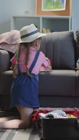 mother and little daughter throw heaps of clothes into suitcase on floor in living room. woman with preschooler girl prepares for journey