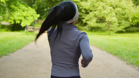 Rear-View-Of-Young-Woman-Exercising-Running-Through-City-Park-Wearing-Wireless-Earbuds