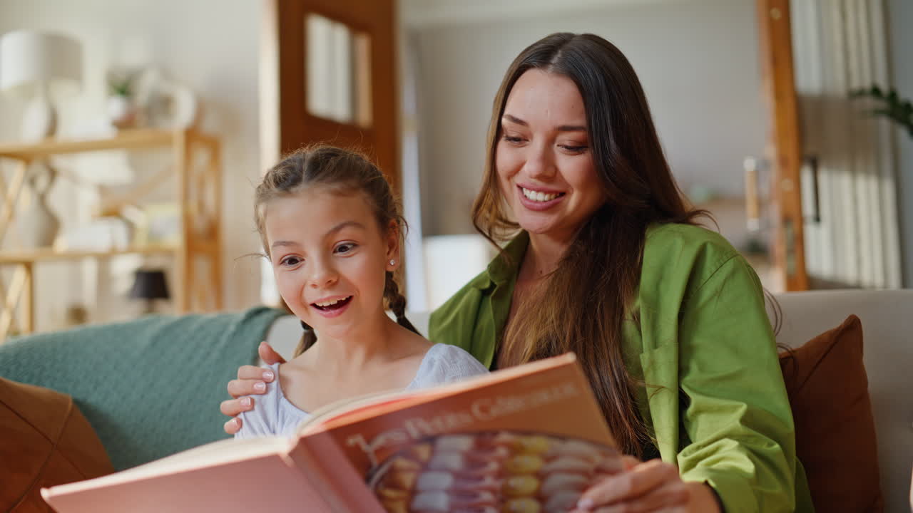 Primo piano di una madre emozionata che comunica con la figlia sul divano. Famiglia felice che legge