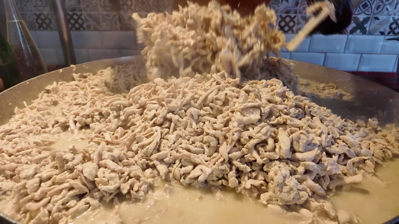 Chef Stirring Shredded Chicken in a Large Pan