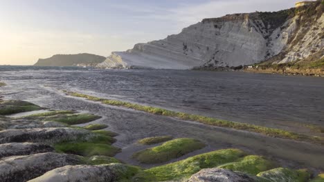 scala dei turchi in argigento, sicily at romantic sunset with water waves and stones with green moss