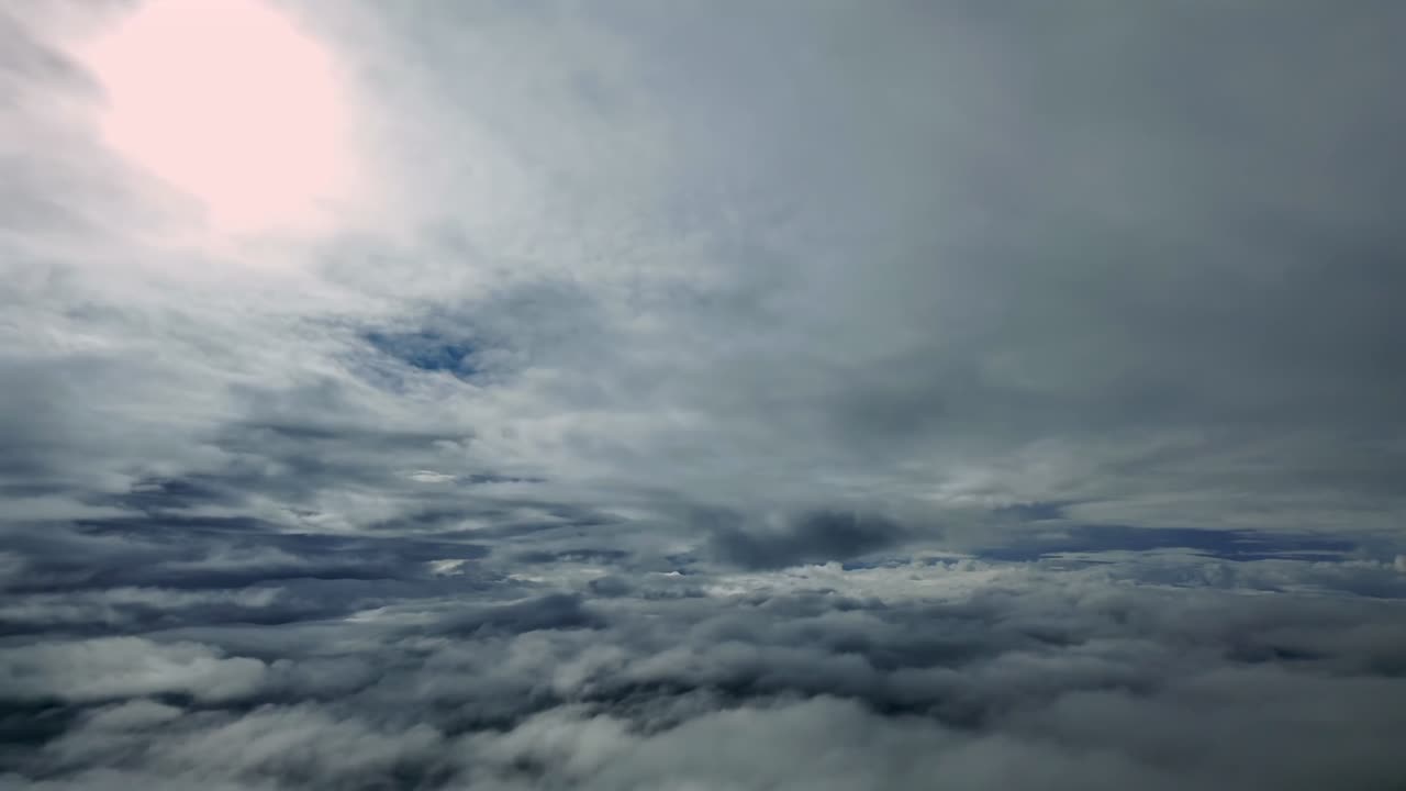 Immersive cockpit view taken from a jet airplane flying through layers of endless ethereal stratus clouds, with a faded sun veiled above in the sky