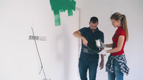 Una-Mujer-Vierte-Pintura-En-Una-Bandeja-Cerca-De-Un-Hombre-Pintando-La-Pared-De-La-Habitación