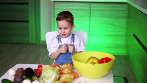 child loves veggies in kitchen. a young child smiles while holding a cabbage, surrounded by colorful vegetables in a bright kitchen
