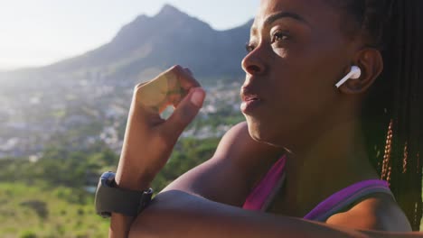 African-american-woman-wearing-wireless-earphones-stretching-her-arms-outdoors