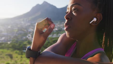 mujer afroamericana con auriculares inalámbricos estirando los brazos al aire libre