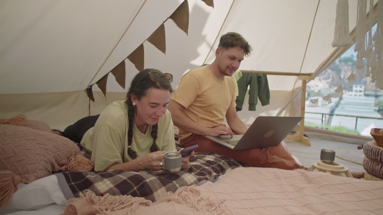 Couple Resting with Laptop and Phone in Glamping Tent