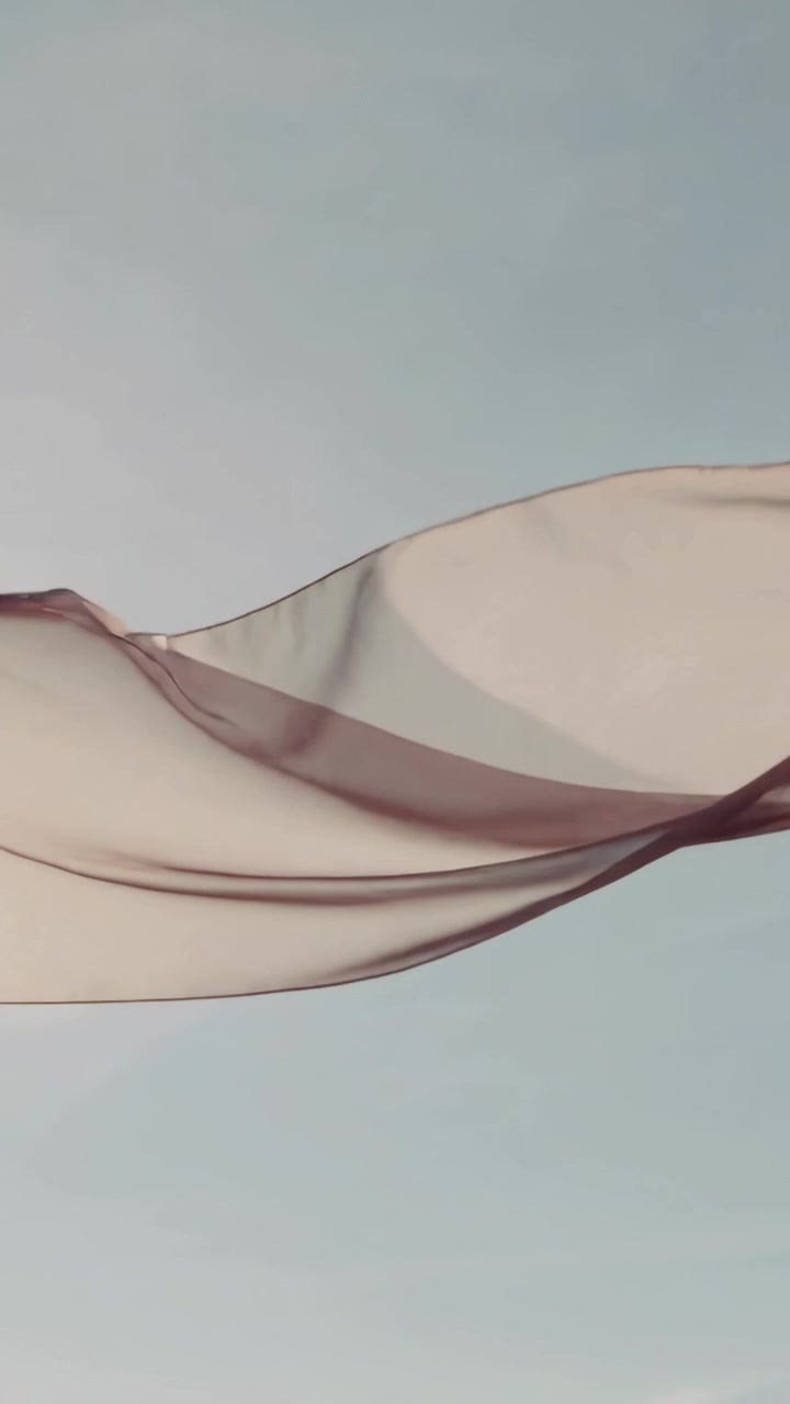 Vertical video: Rising large translucent fabric floating across pale blue sky, driven by breeze