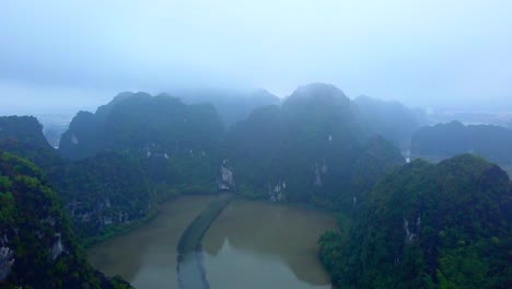 cinematic drone footage of majestic limestone peaks in misty and foggy weather. ricefields in wild jungle in the spring with boat tour canal in tam coc, ninh binh, vietnam