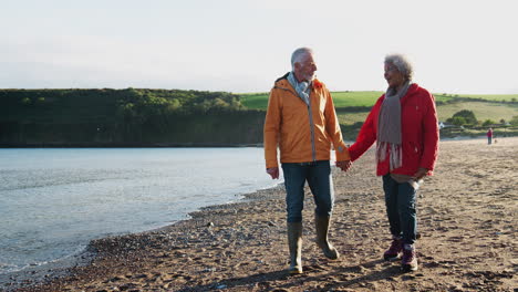 Amorosa-Pareja-De-Ancianos-Activos-Tomados-De-La-Mano-Mientras-Caminan-Por-La-Costa-En-Vacaciones-De-Invierno-En-La-Playa