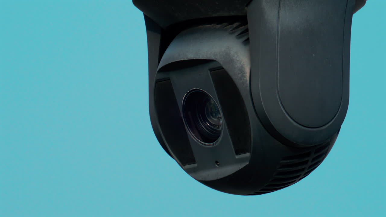 A close up of a modern black surveillance camera turning against a bright sky background