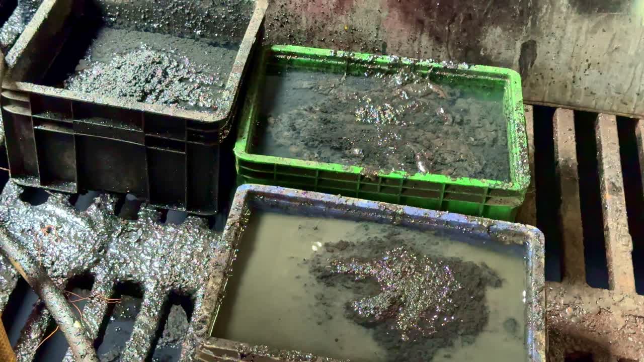 Close-up view of industrial wastewater sludge collected in plastic containers, showing polluted water and sediment from factory waste treatment