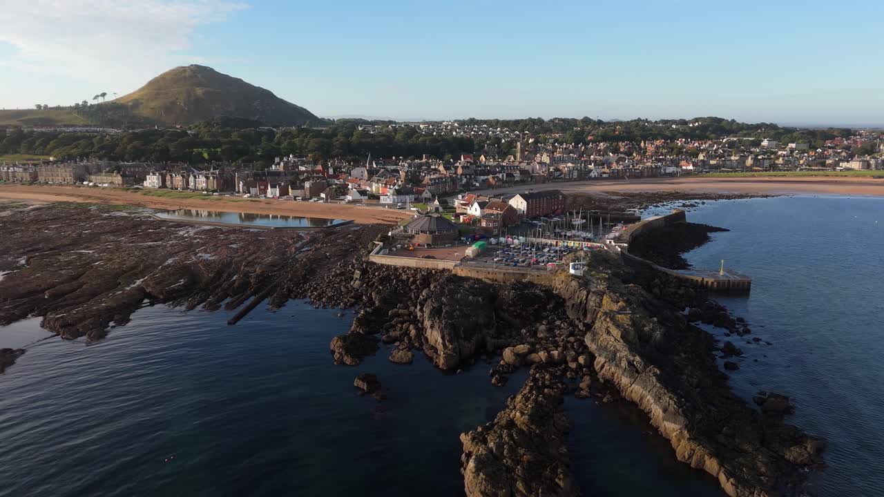 Aerial footage of North Berwick, Scotland in golden morning sunlight. stunning views of the town’s historic harbour, sandy beaches, and rugged coastline along the North Sea