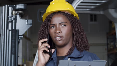 primer plano de una trabajadora afroamericana hablando por teléfono, de pie en el almacén y sosteniendo un portapapeles