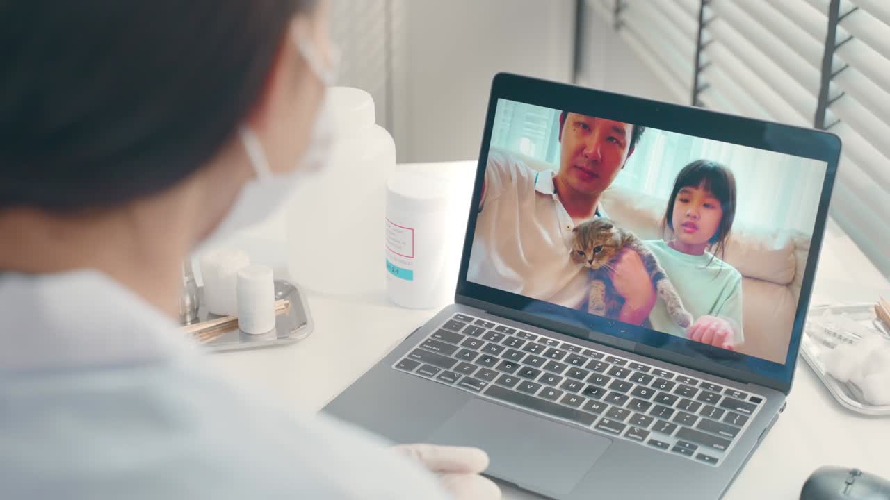 Asian veterinarian girl talk to pet owner on online virtual video call. Professional vet doctor woman use laptop computer to give treatment plan consult for little cat animal while sit in pet hospital