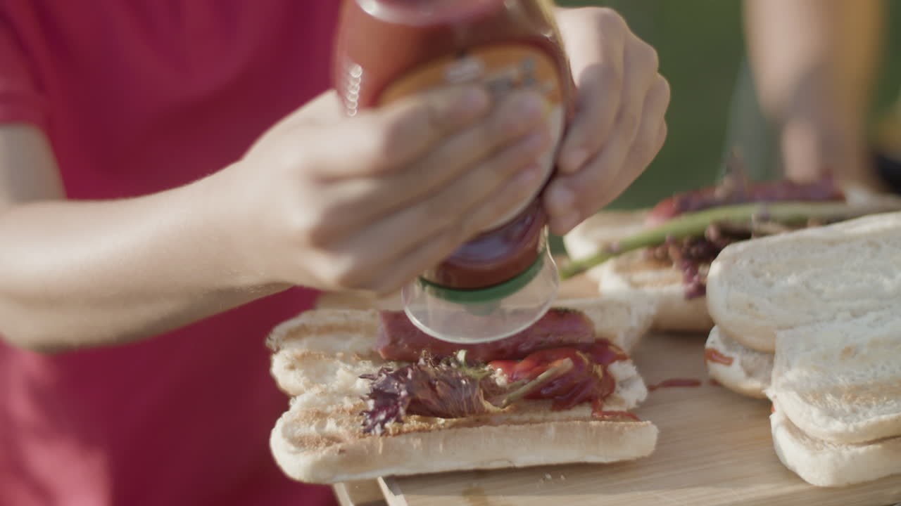 Primo piano di un ragazzo che spreme il ketchup su un hotdog all'aperto.