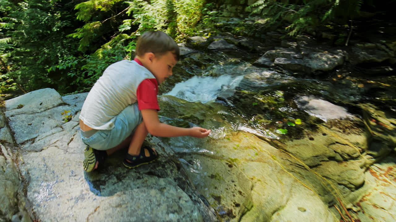 어린 소년은 자연 공원, 브리티시 컬럼비아 캐나다의 바위 절벽 꼭대기에서 폭포  ⁇ 에 앉아 있습니다.