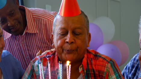 senior man blowing out the candles on a birthday cake with his friends 4k