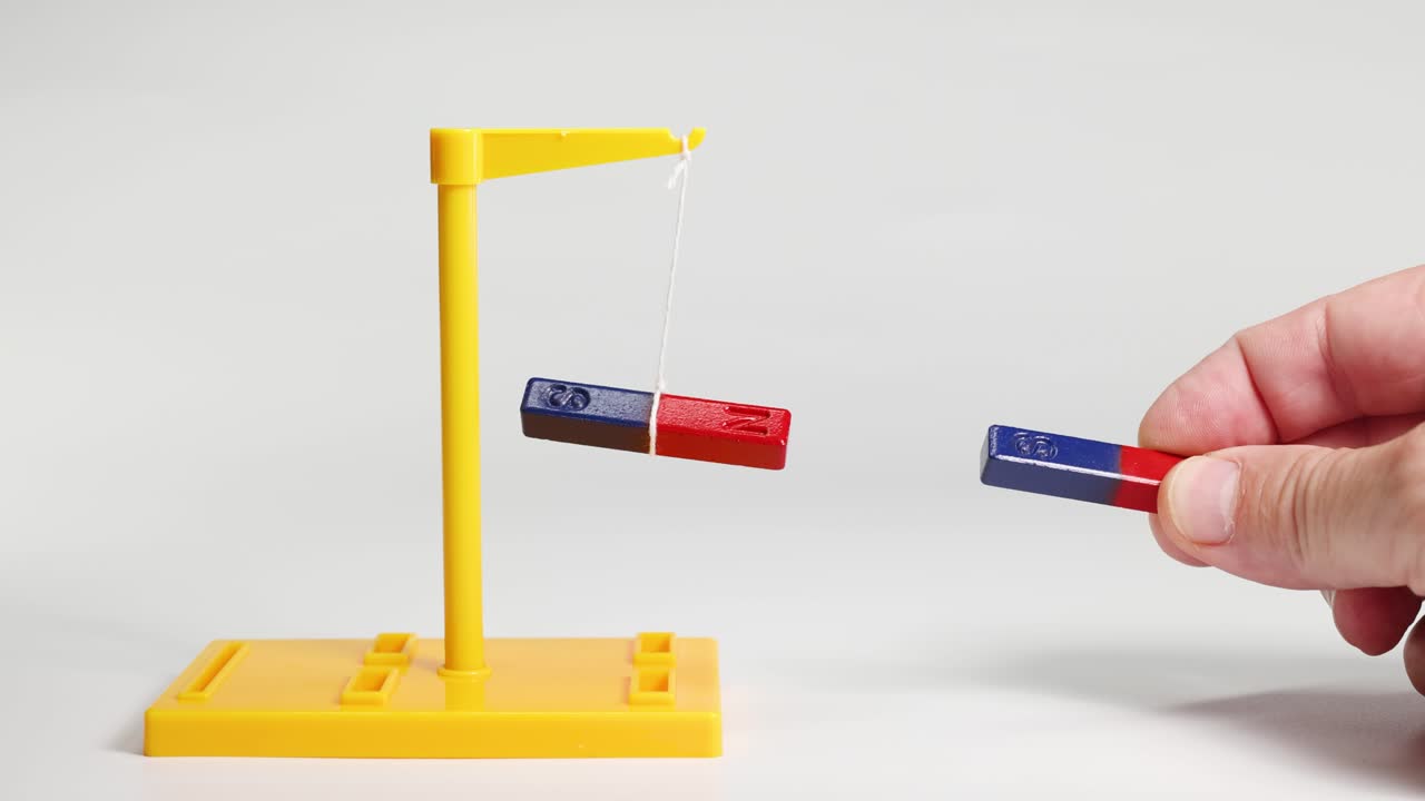 A hand manipulates magnets, demonstrating attraction and repulsion. Bright lighting highlights the magnetic forces in a controlled environment