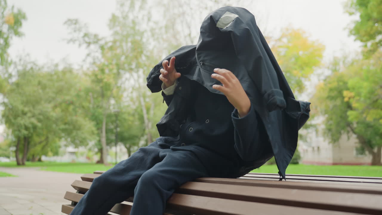 Ceketiyle başını örten, kapüşonunu aşağı çekip park bankında ayarlayan, sonra yorgun bir şekilde dinlenmeye çöken bir öğrenci, sonbahar ağaçları ve sakin bir patika, geri dönmeden önceki savunmasızlığın ham anı.