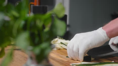 calabacín fresco cortado en una tabla de madera por un joven chef profesional con un elegante pantalones negro con tatuajes