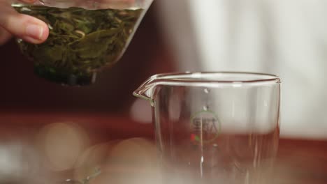 pouring infused green tea from gaiwan bowl into the glass on traditional dark wood tea table