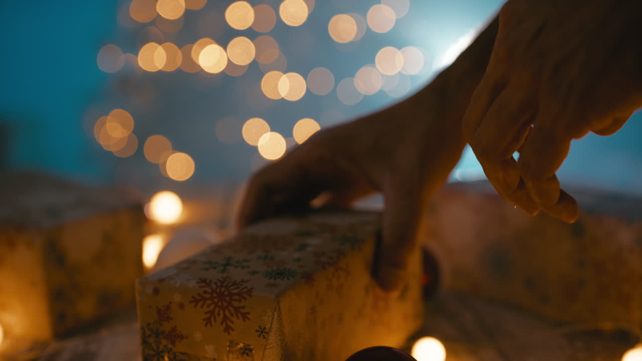 A man hand arranges Christmas presents on the table in front of the tree