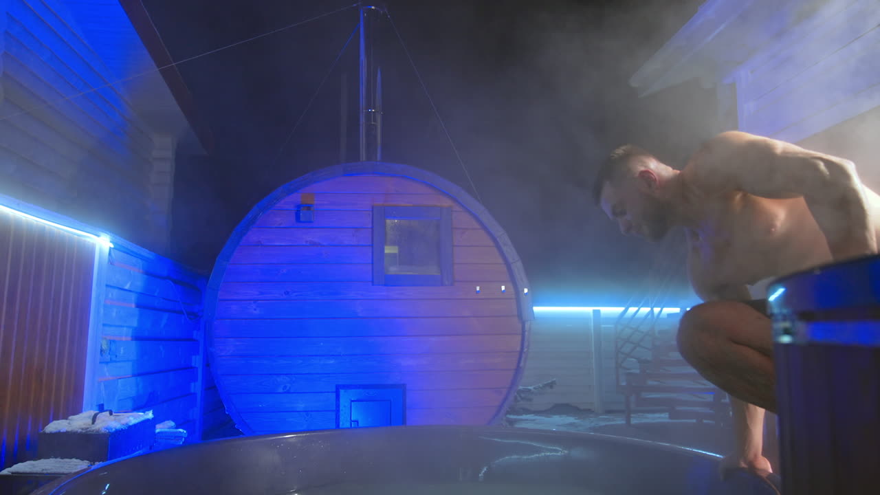 Muscular man wearing shorts comes up to the hot tub. Man gets into Jacuzzi and sits down comfortably.