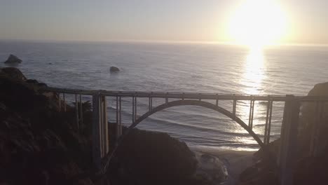 aerial drone shot of bixby bridge with road and ocean sunset