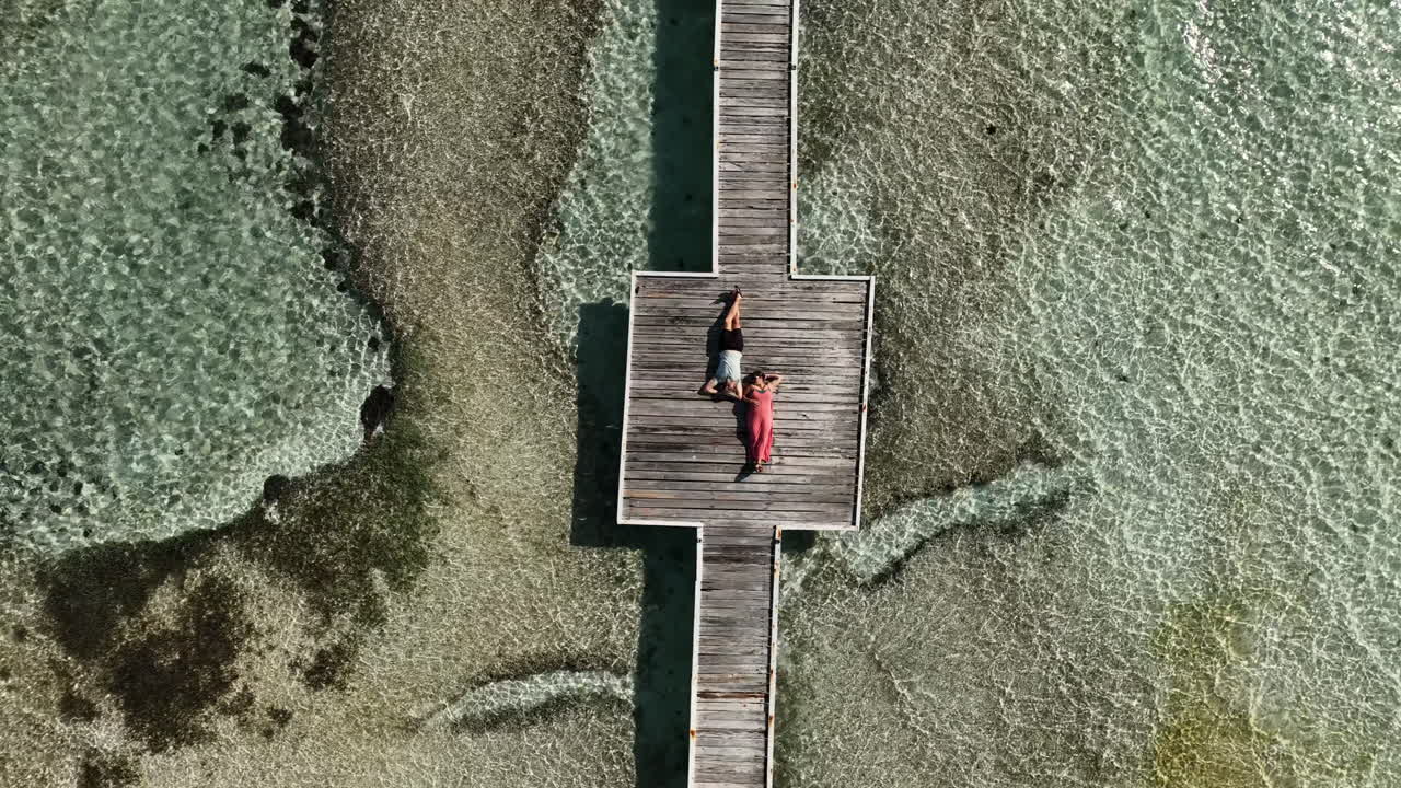 Top down ascending aerial view of couple laying on pier in the Caribbean.
