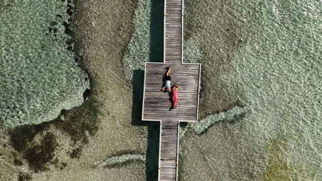 top down ascending aerial view of couple laying on pier in the caribbean.