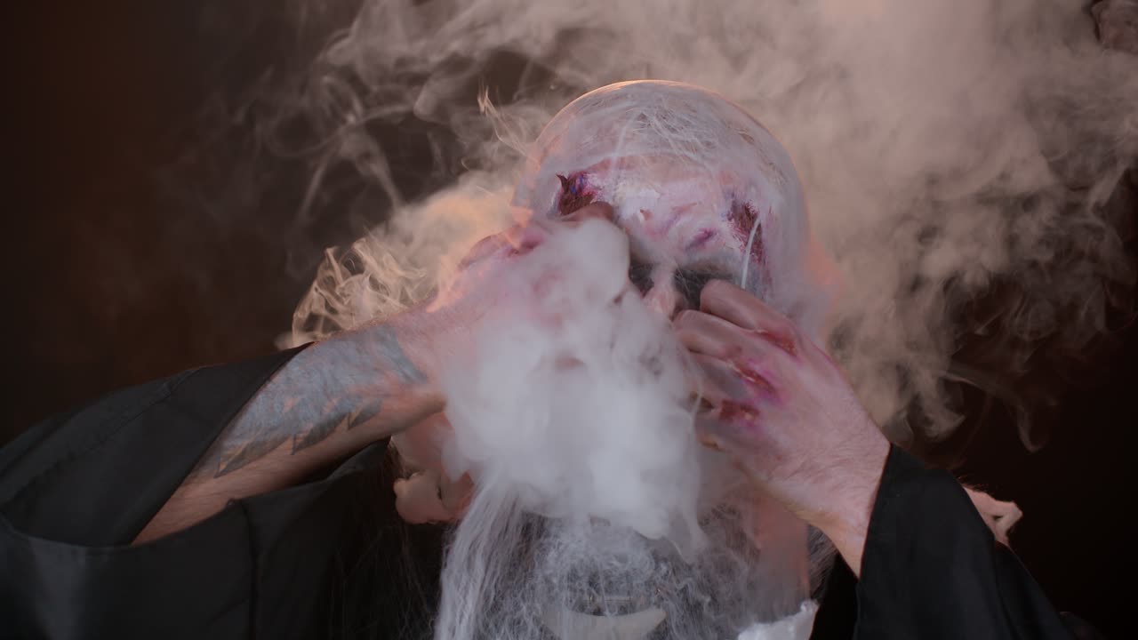 hombre aterrador halloween zombie sangriento herido escondiéndose detrás de las manos sopla humo de la nariz y la boca