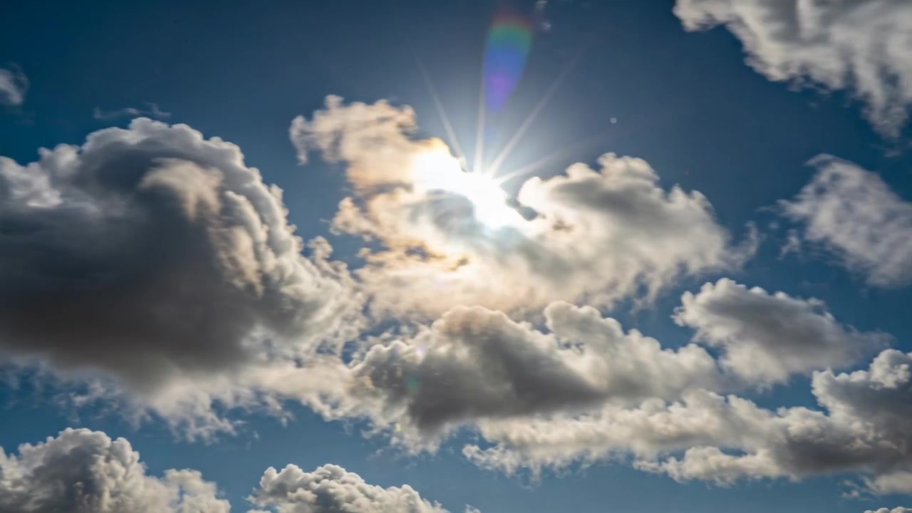 Shifting cumulus cloud uncovering sun from ground revealing glare and lens flare driven by wind