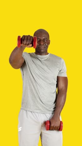 senior man exercising with dumbbells on yellow background