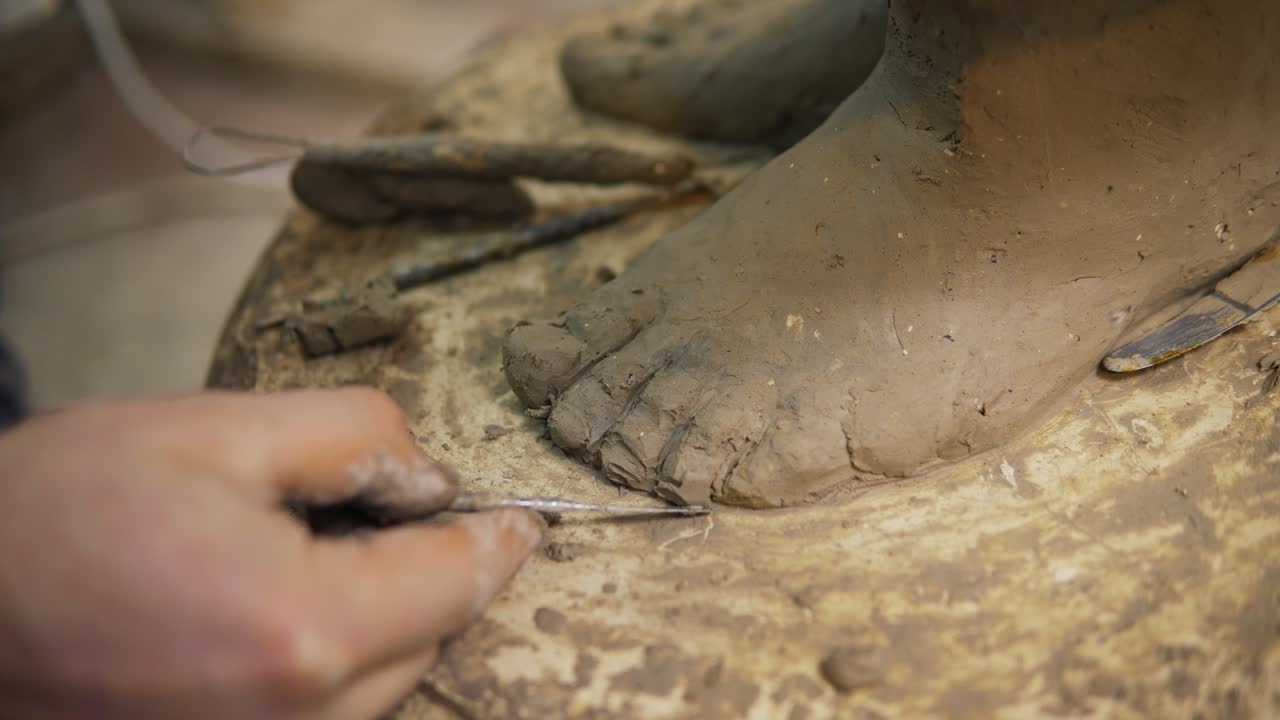 Close up of clay Buddha's statue feet, artist works with detail using spatula