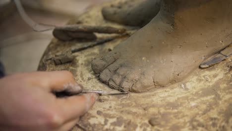 Close-up-of-clay-Buddha's-statue-feet,-artist-works-with-detail-using-spatula