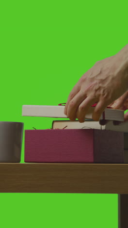 vertical video of man opening present in gift wrapped box on table shot against green screen