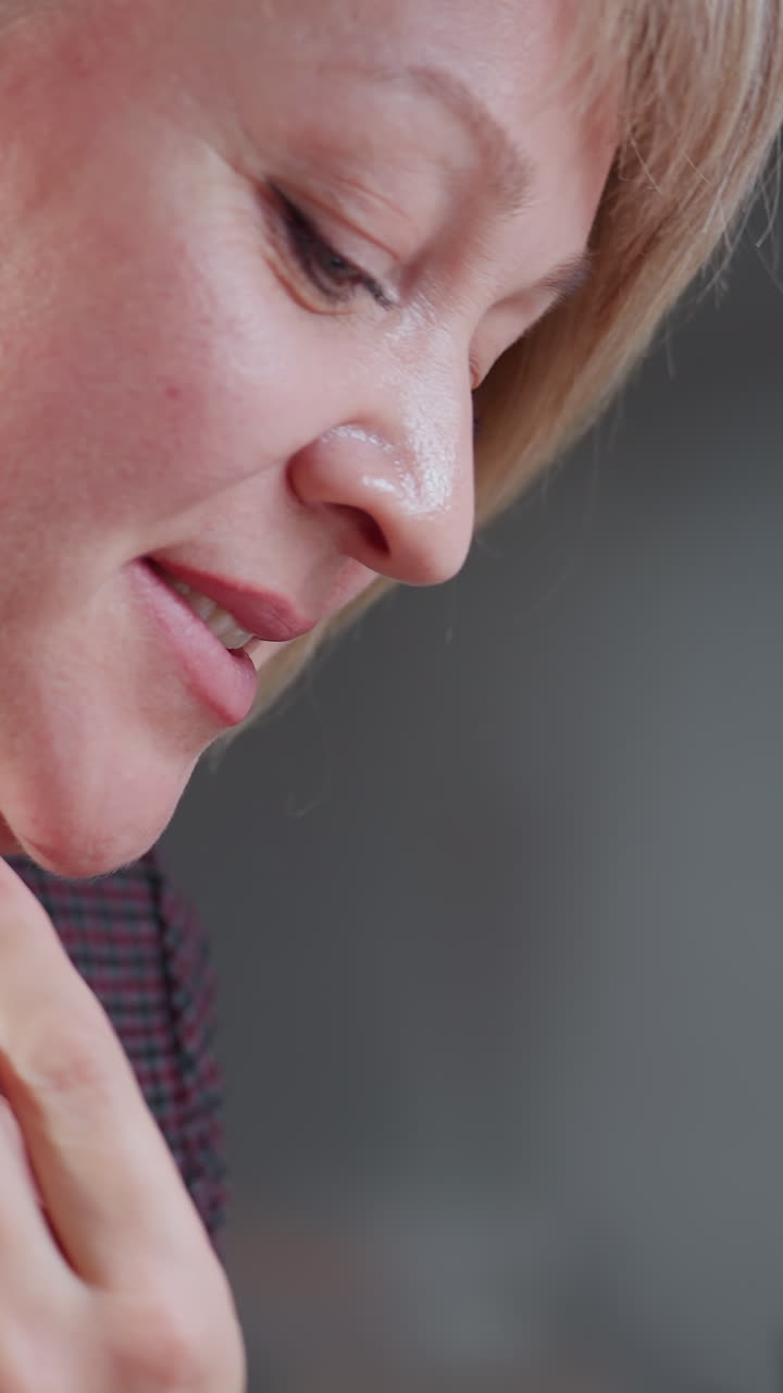 mujer de cabello rubio corto cocinando en una cocina moderna, inclinándose para oler el aroma de la comida con una sonrisa satisfecha, mano en el cuello adornada con una pulsera de cuentas rosas, sosteniendo un cucharón y tofu en el plato
