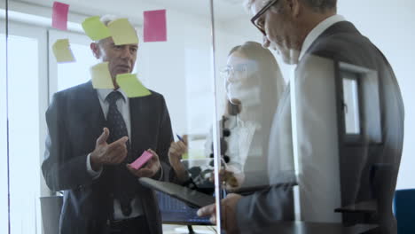 equipo de negocios de diferentes edades pegando notas de papel en una pared transparente