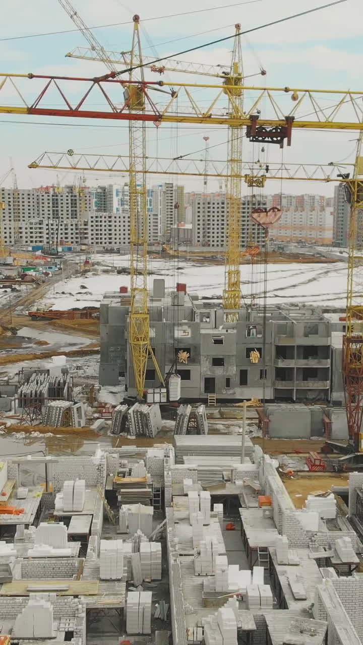unfinished project with white buildings and large construction cranes against residential blocks and blue sky upper view