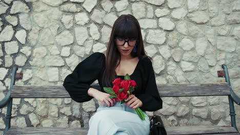 woman on a wooden bench admiring the red flowers gift from her love