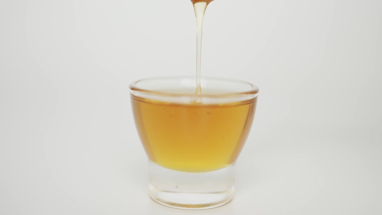 Primo piano, miele che cola da un mestolo per miele in un bicchiere