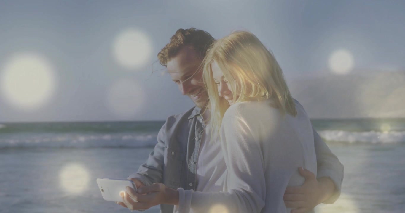 Coppia appoggiata sulla riva dell'oceano, che naviga contenuti tecnologici su tablet mentre la luce del sole si diffonde dolcemente.