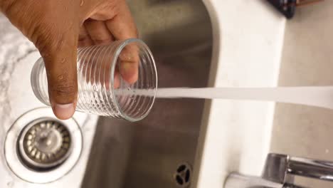 persona llenando un vaso con agua de un grifo de la cocina