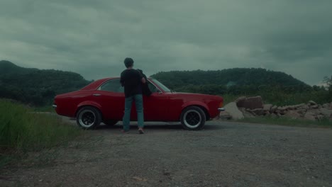 man walking away from red classic car on a gravel road