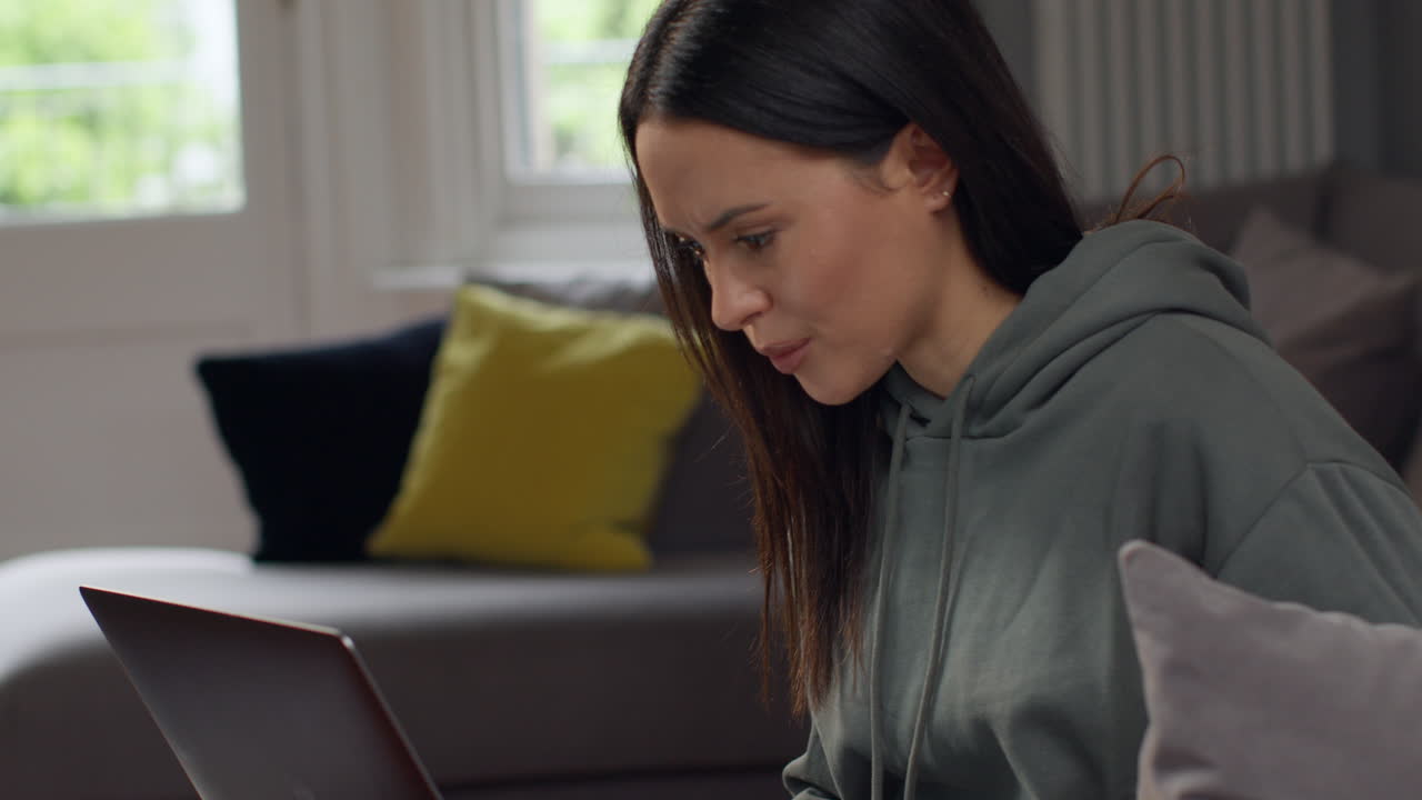 mujer ansiosa sentada en el sofá trabajando desde casa usando una computadora portátil preocupada por la crisis del costo de la vida 1
