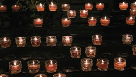 filas de velas de oración rojas en una iglesia