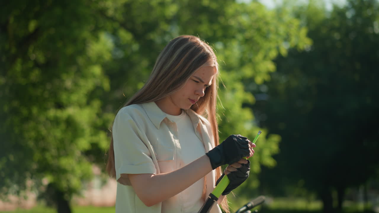 금발 머리카락을 가진 젊은 여성이 초록색 공기 프와 노즐을 집중적으로 조사하고 그녀의 장갑을 입은 손으로 울창한 나무와 초록색의 배경에 서 있습니다.