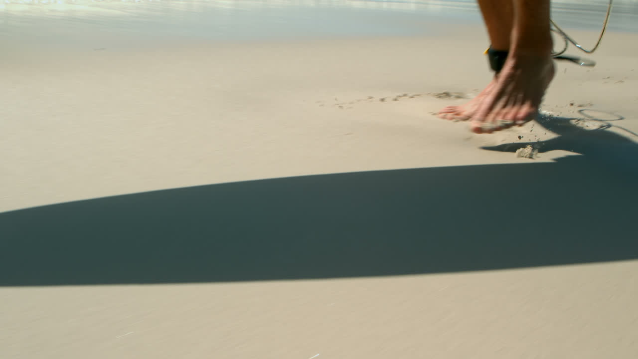 해변 4k에서 발목에 서프보드  ⁇ 을  ⁇ 고 달리는 남자의 낮은 섹션