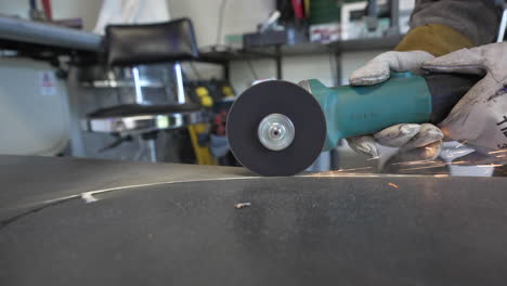 person cutting steel plate using an electric grinder with sparks at the workshop